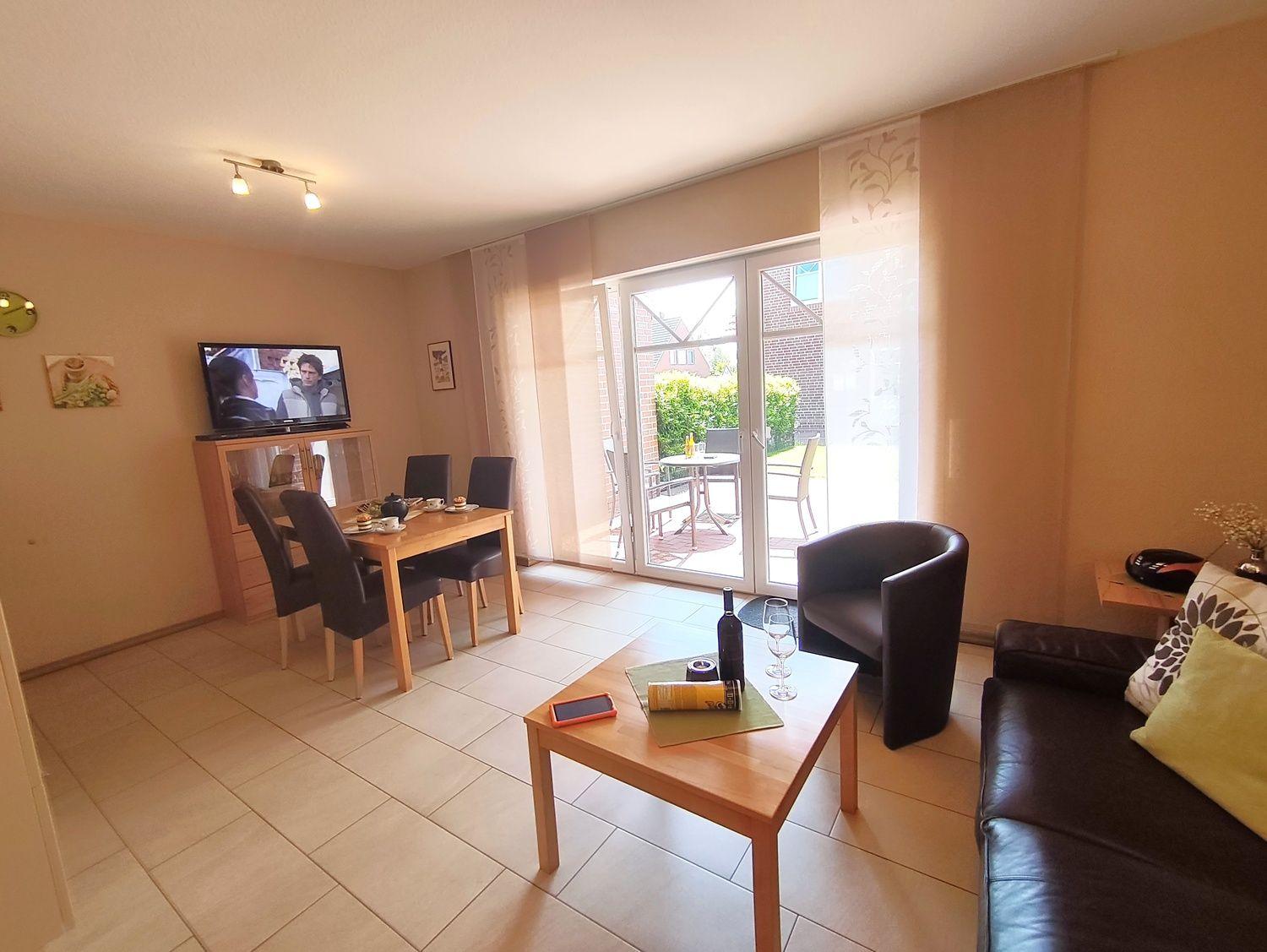 Wohn- und Essbereich mit Fernseher, Tisch, Stühlen und Terrasse.