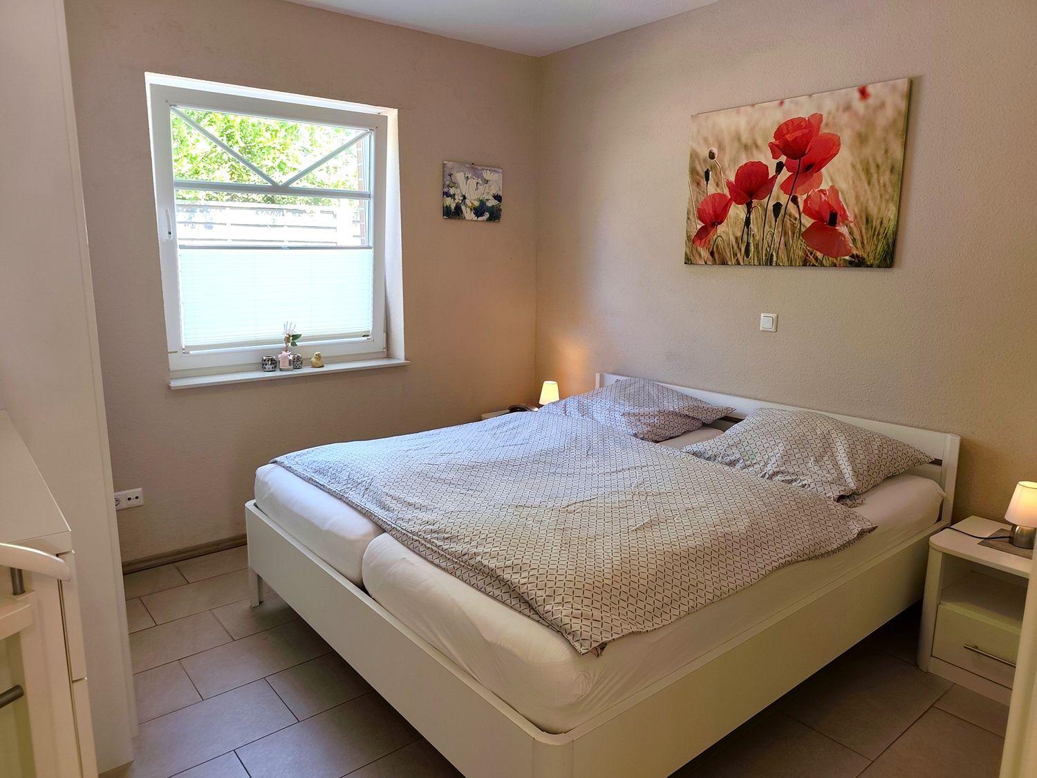 Schlafzimmer mit Doppelbett, Fenster und Wandbild mit roten Mohnblumen.