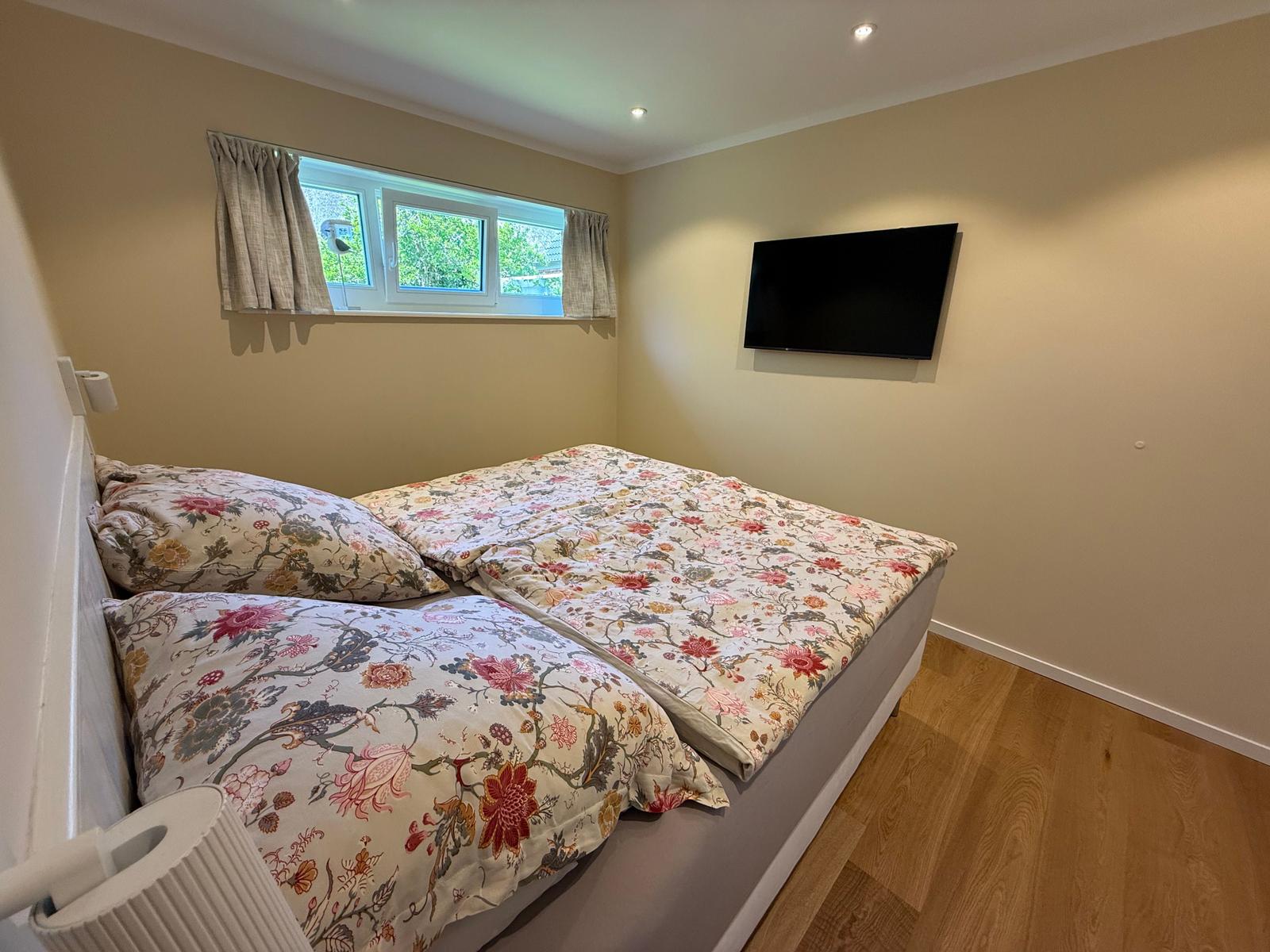 Schlafzimmer mit Bett, Fenster und Wandfernseher