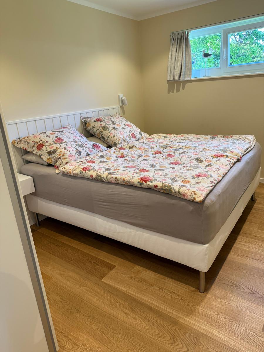 Schlafzimmer mit Doppelbett, Holzboden und Fenster mit Blick auf Grün.