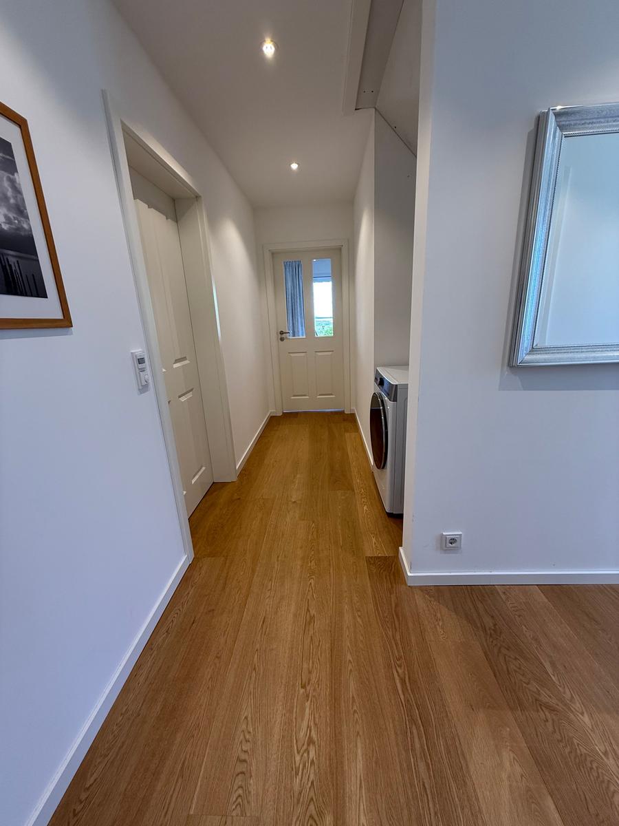 Flur mit Holzboden, Waschmaschine und Spiegel an der Wand.