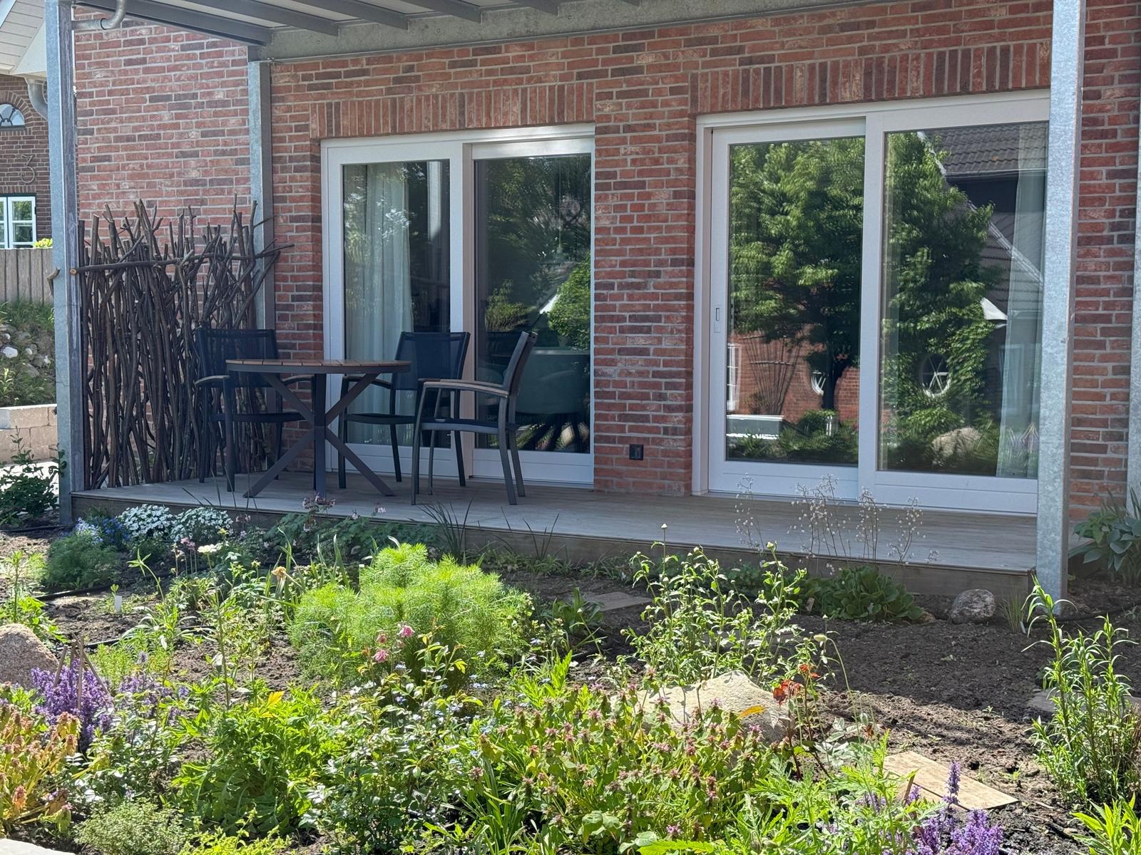 Terrasse mit Tisch und Stühlen vor rotem Backsteinhaus mit Gartengrün.