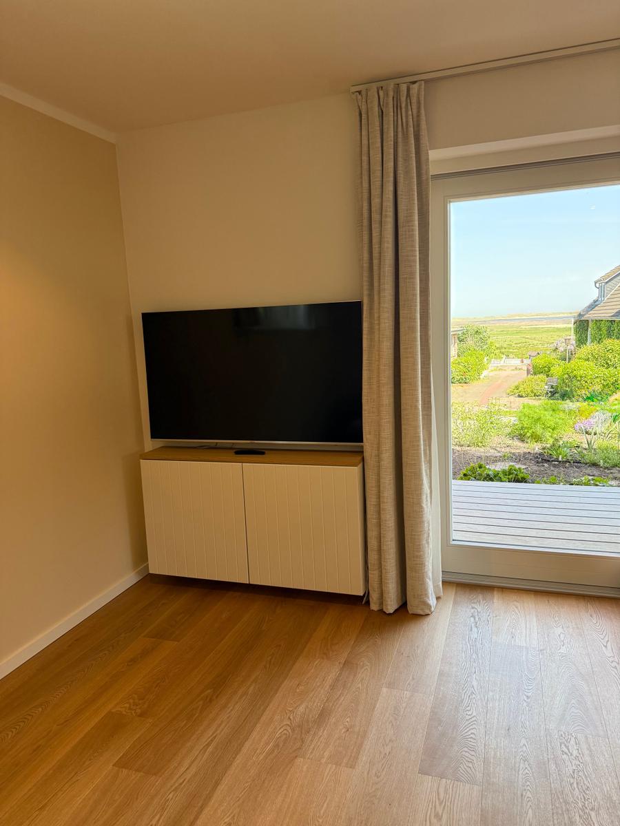 Ein Raum mit Fernseher, Holzboden und Blick auf einen Garten.