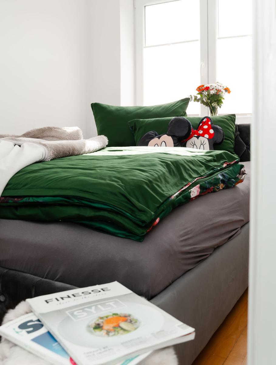Doppelbett mit grünem Bettbezug und Minnie-Mouse-Kissen. Auf dem Bett liegen Zeitschriften.
