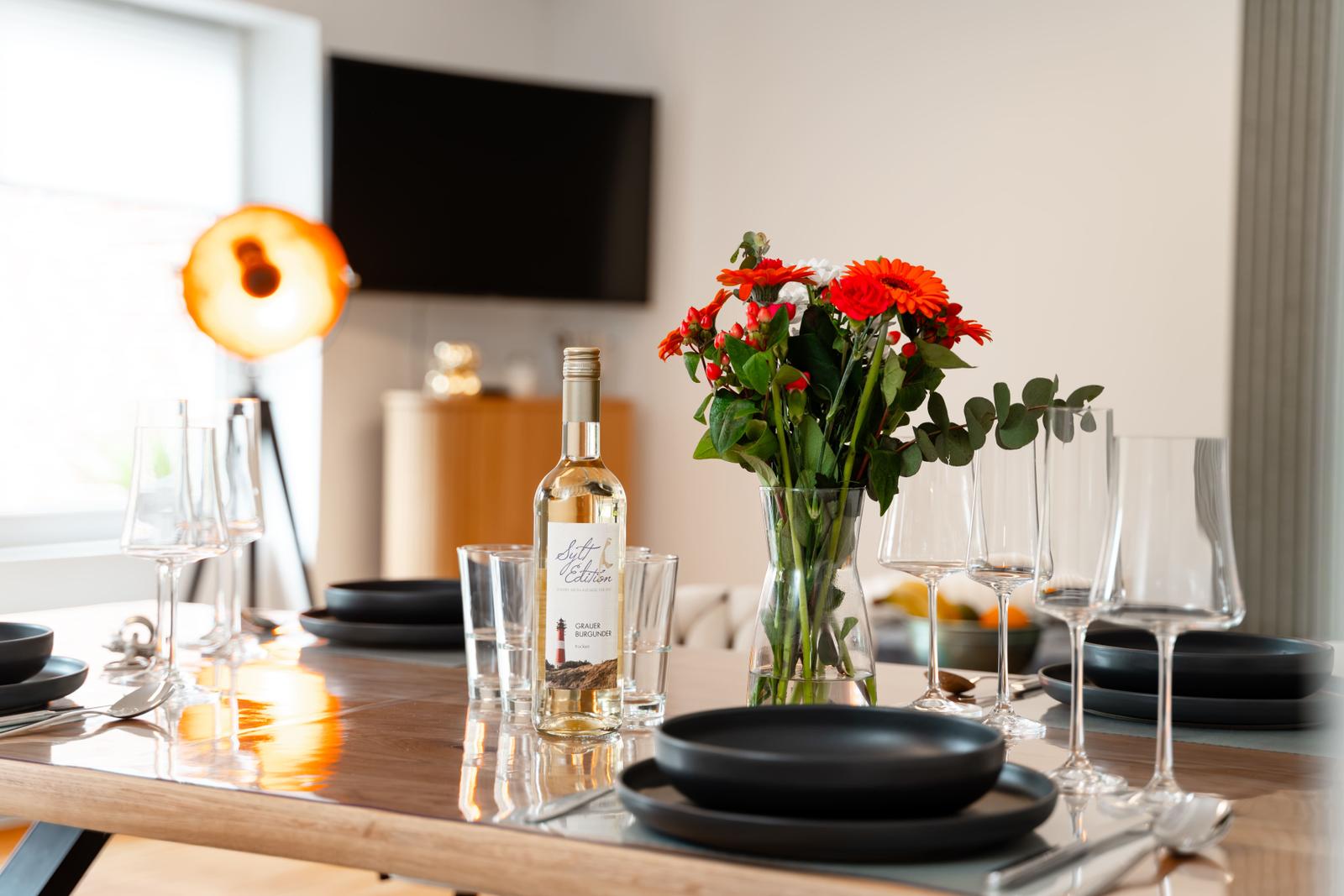Esstisch mit schwarzen Tellern, Weingläsern und Blumenarrangement.