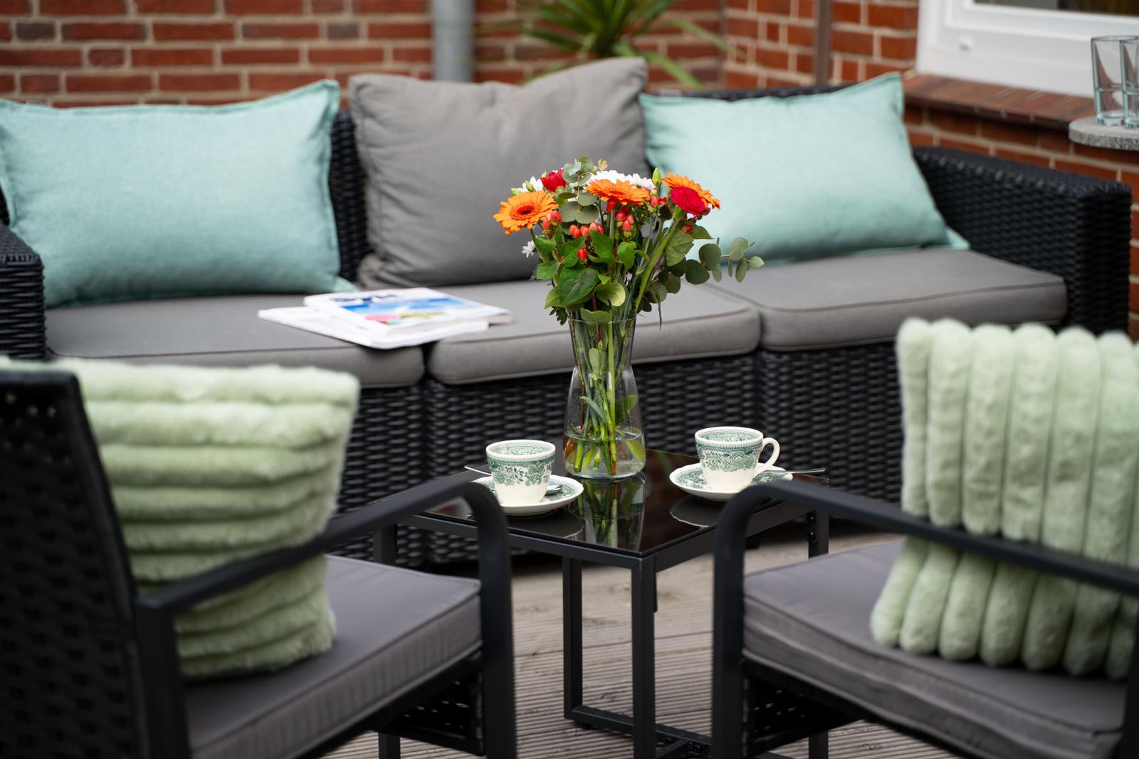 Terrasse mit Sitzgruppe, Blumen und Tassen auf Tisch