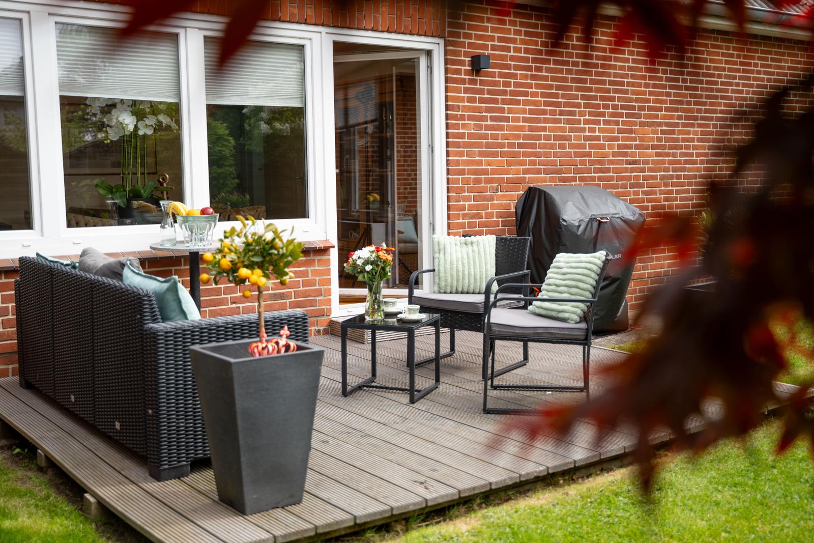 Terrasse mit Sitzgruppe, Pflanzen und Gartentisch vor rotem Backsteinhaus