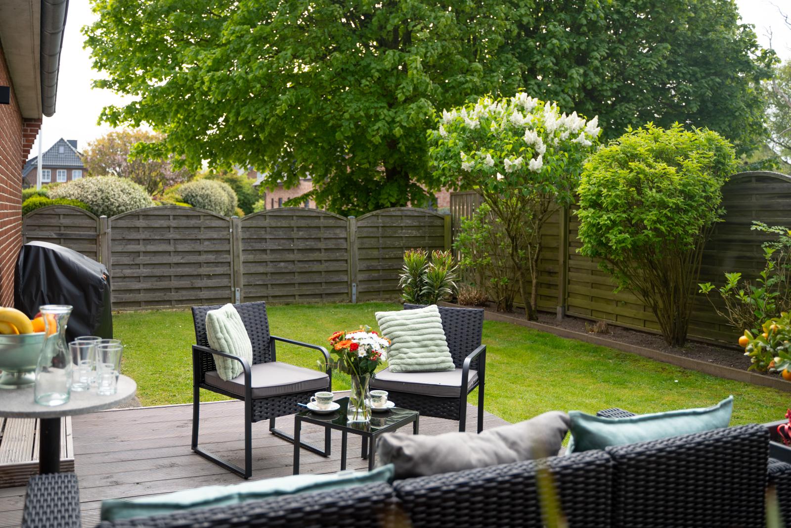 Hinterhof mit Garten, Sitzgruppe und Grillplatz. Grünflächen und Bäume umgeben den Bereich.