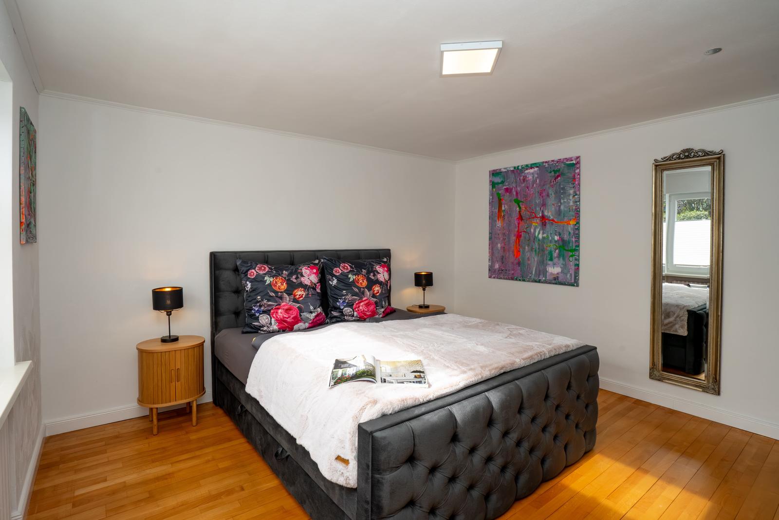 Schlafzimmer mit großem Bett, Holzboden und Wandbildern.