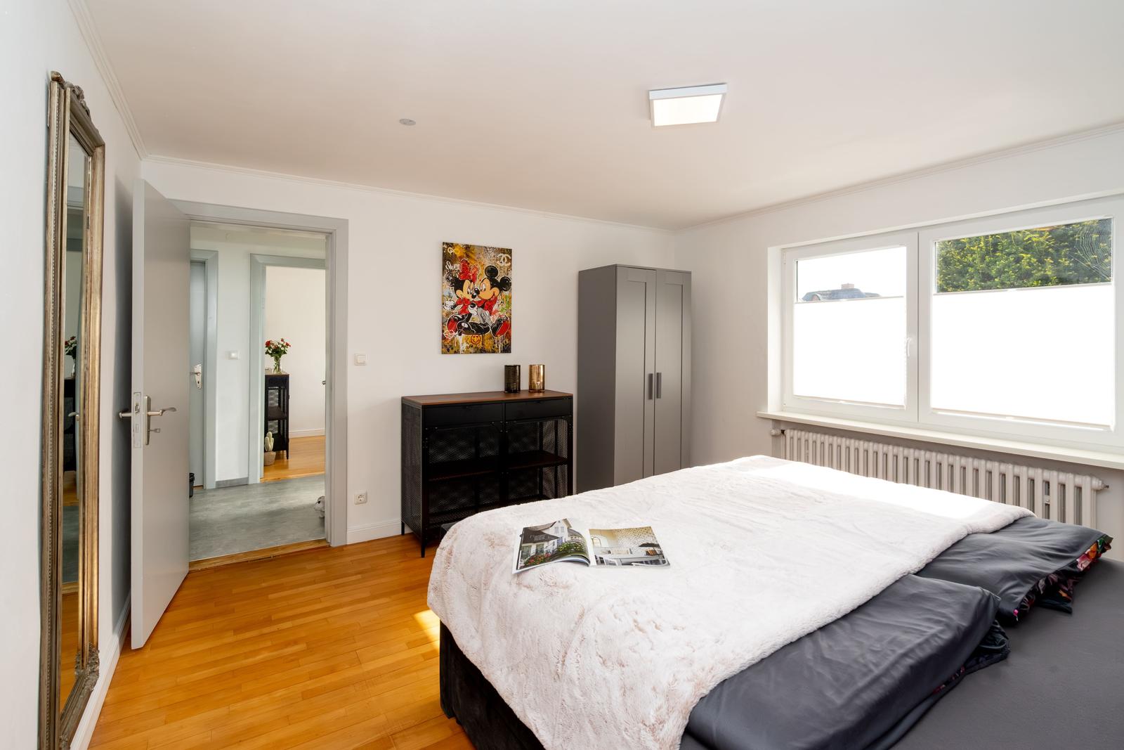 Schlafzimmer mit Bett, Kleiderschrank und Fenster. An der Wand hängt ein Bild.