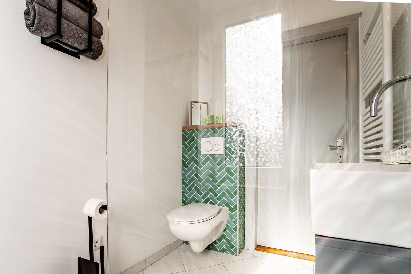 Badezimmer mit Toilette, Waschbecken und grüner Fliesenwand.