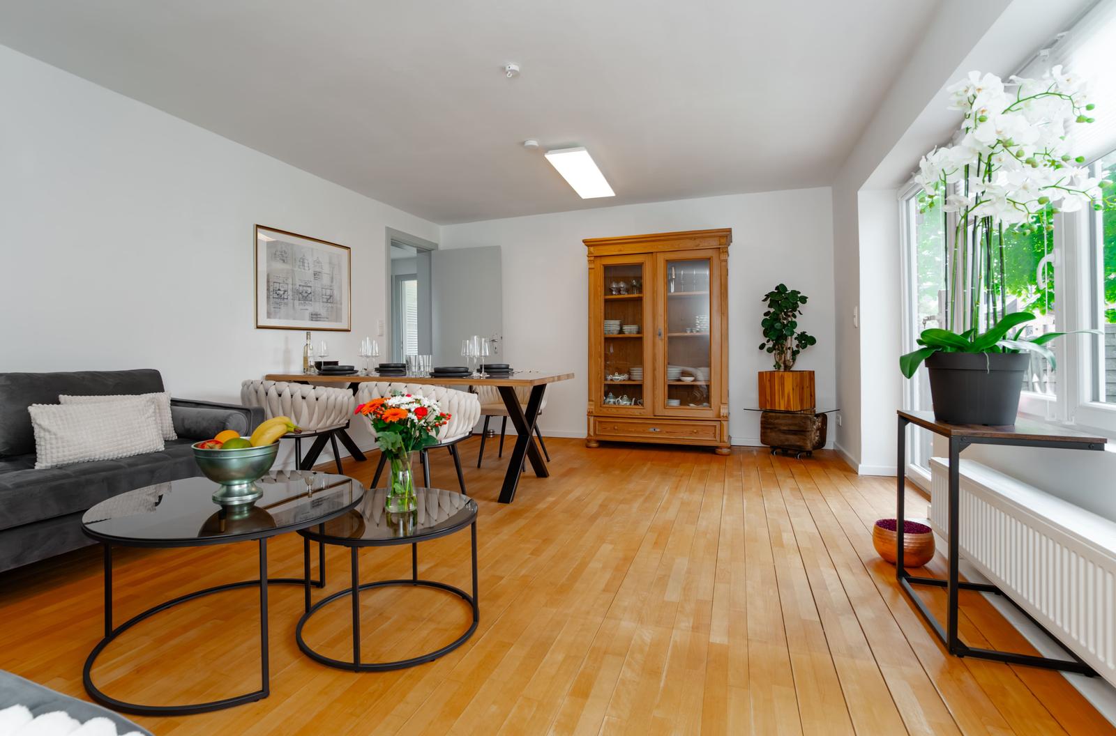 Wohn- und Essbereich mit Holzboden, Sofa, Tisch und Pflanzen.