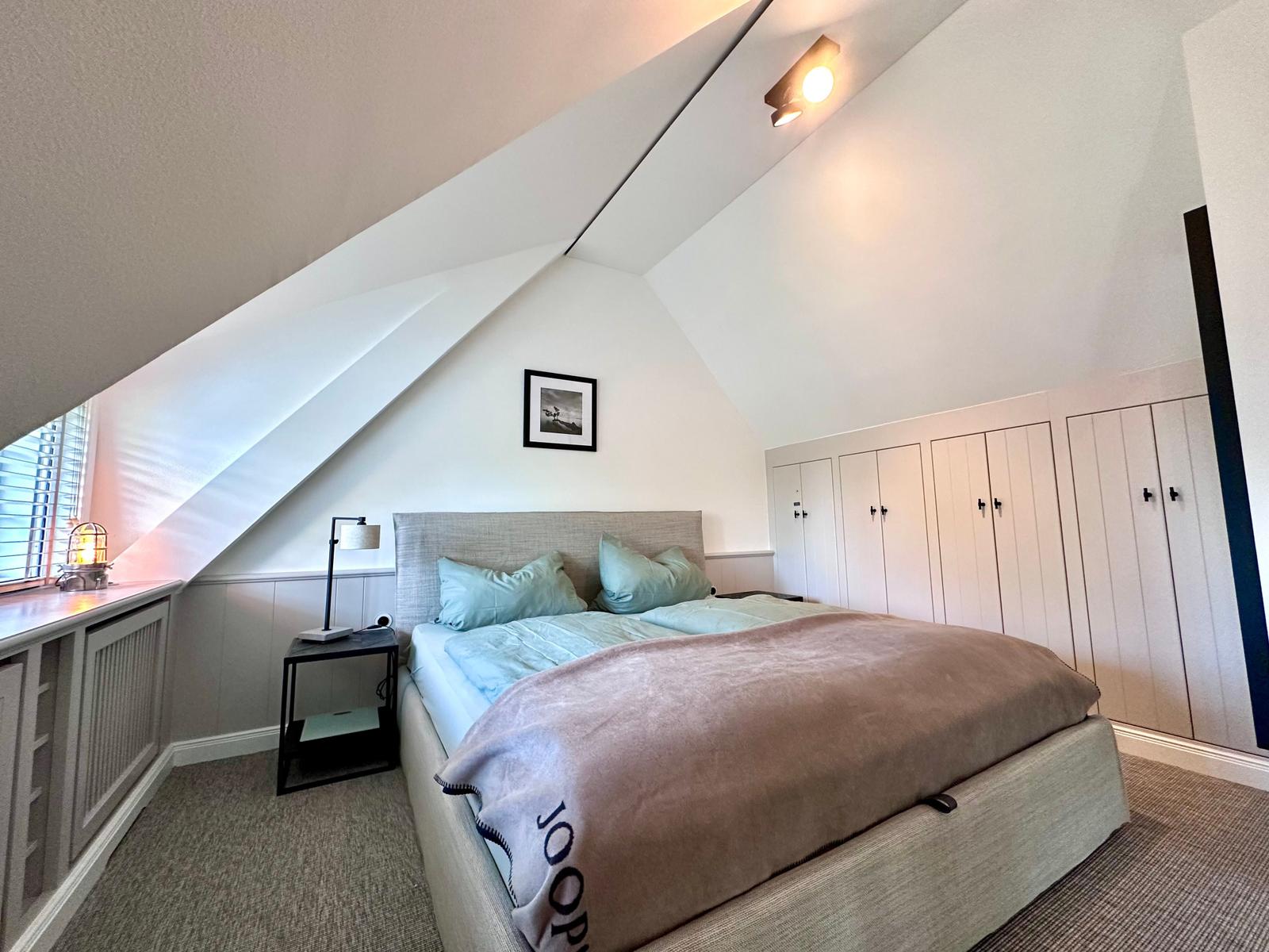 Schlafzimmer mit Dachschräge, Bett, Kleiderschrank und Nachttisch.