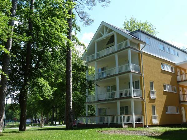 Gelbes Mehrfamilienhaus mit weißen Balkonen und umliegenden Bäumen.