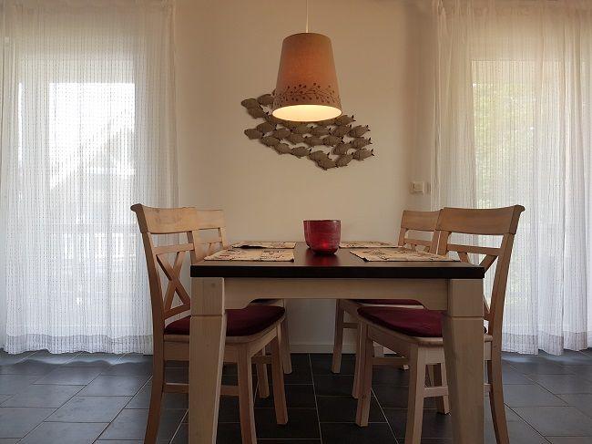 Esszimmer mit Holztisch, vier Stühlen und Deckenleuchte. Fenster mit weißen Vorhängen.