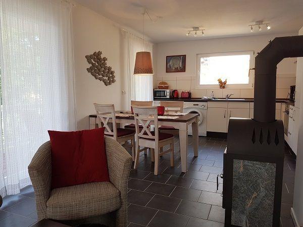 Essbereich mit Tisch, Stühlen und Kaminofen. Küche mit Waschmaschine und Fenster.