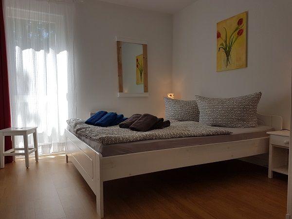 Schlafzimmer mit weißem Bett, Wandbild und Fenster mit Vorhängen.