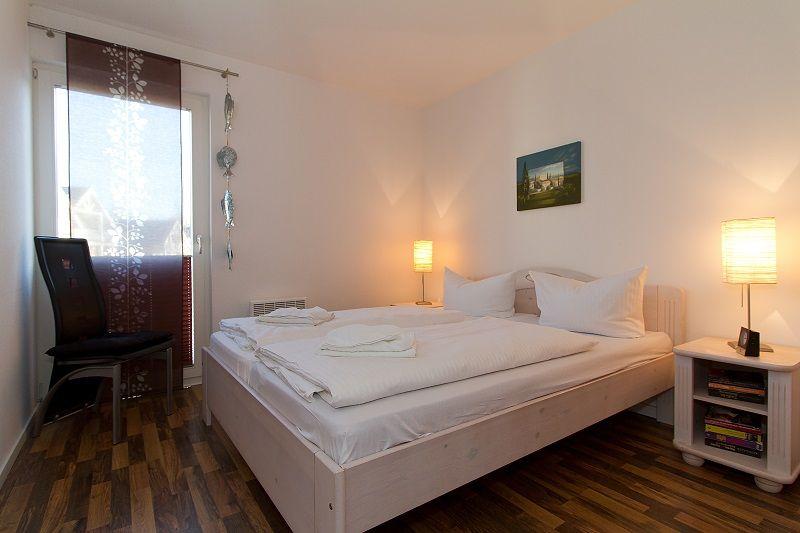 Schlafzimmer mit Bett, Nachttisch und Fenster mit Vorhang.
