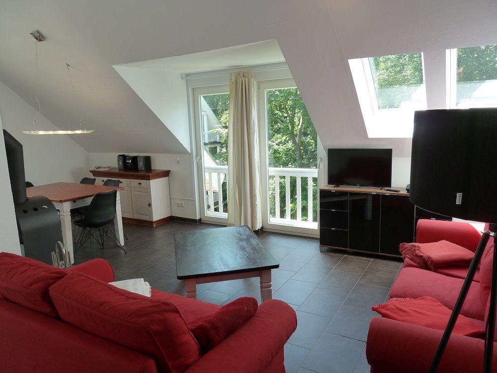 Wohn- und Essbereich mit roten Sofas, TV und Balkon. Dachgeschoss mit Fenstern und Türen.