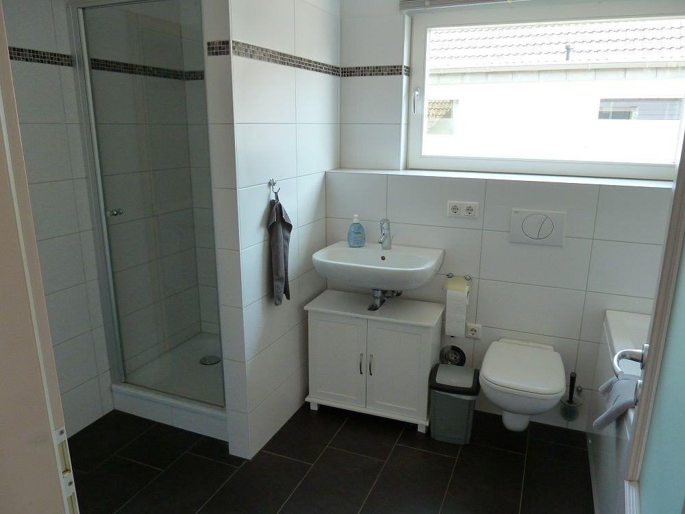 Badezimmer mit Dusche, Waschbecken und Toilette. Fenster sorgt für Tageslicht.