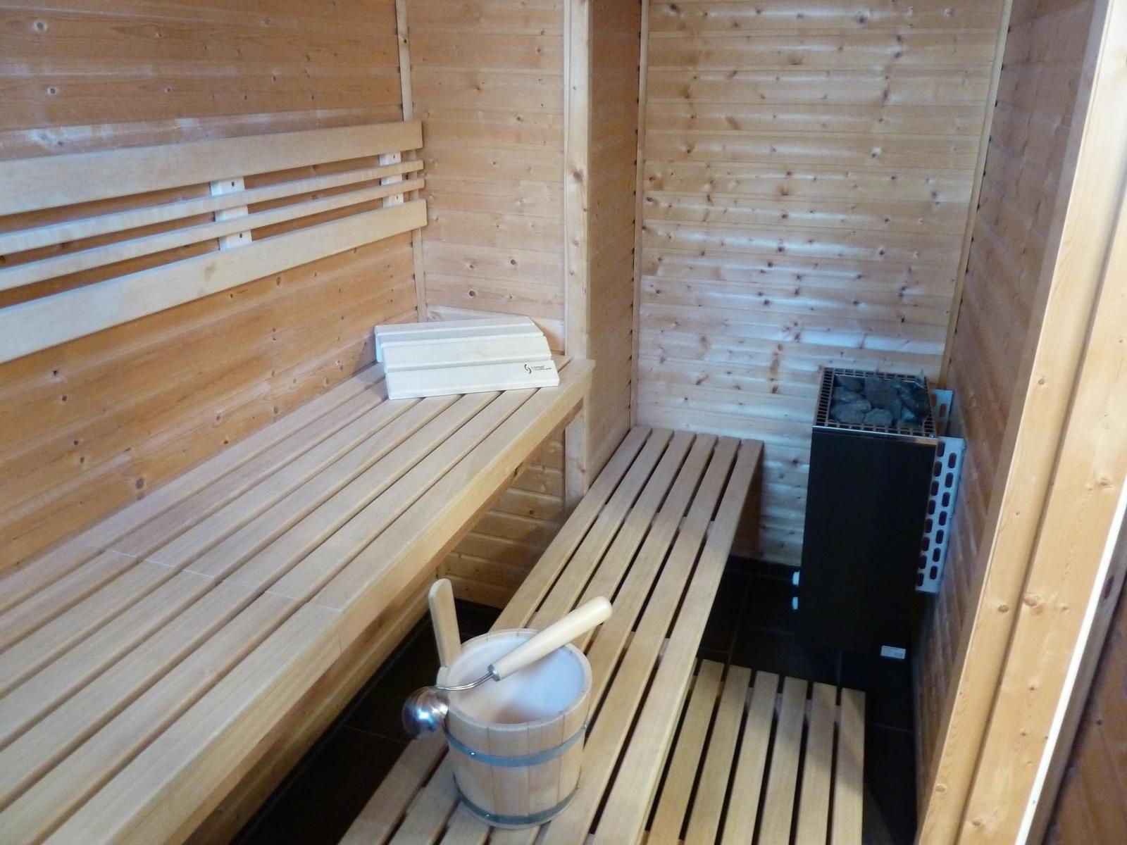 Sauna mit Holzbank, Steinkachelofen und Eimer mit Löffel.