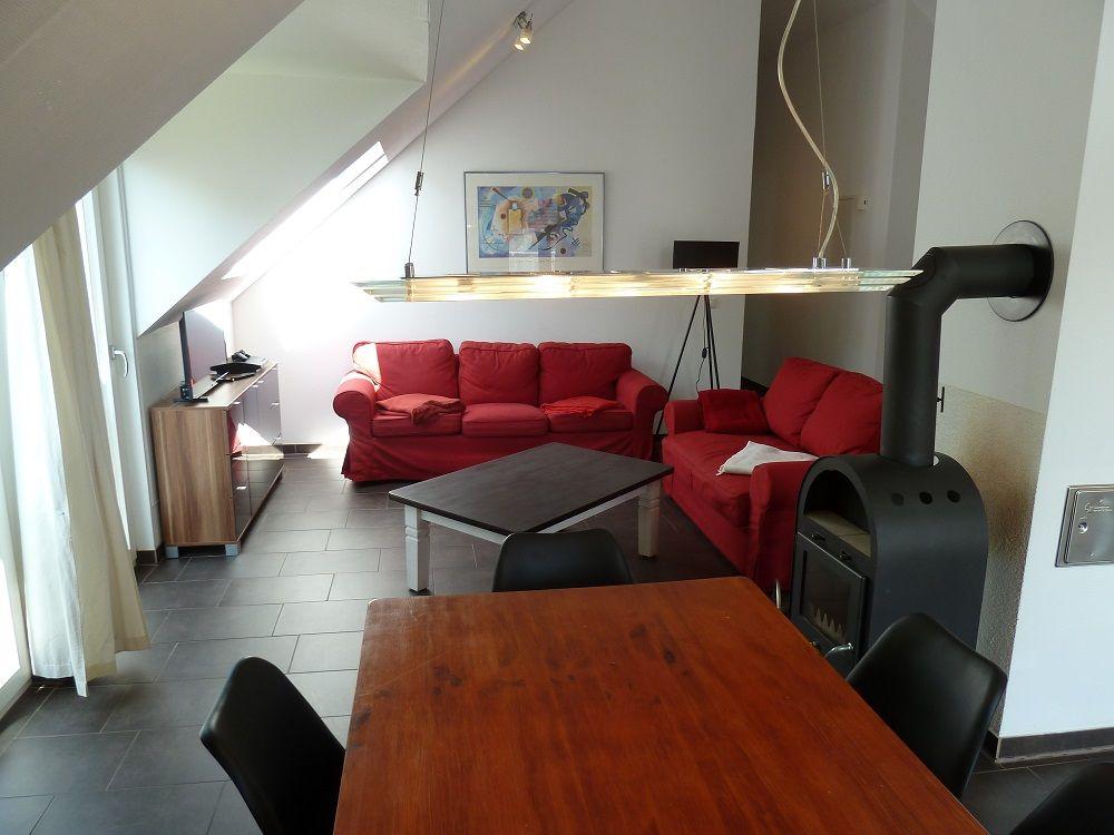 Wohn- und Essbereich mit rotem Sofa, Esstisch und Kaminofen unter Dachschrägen.