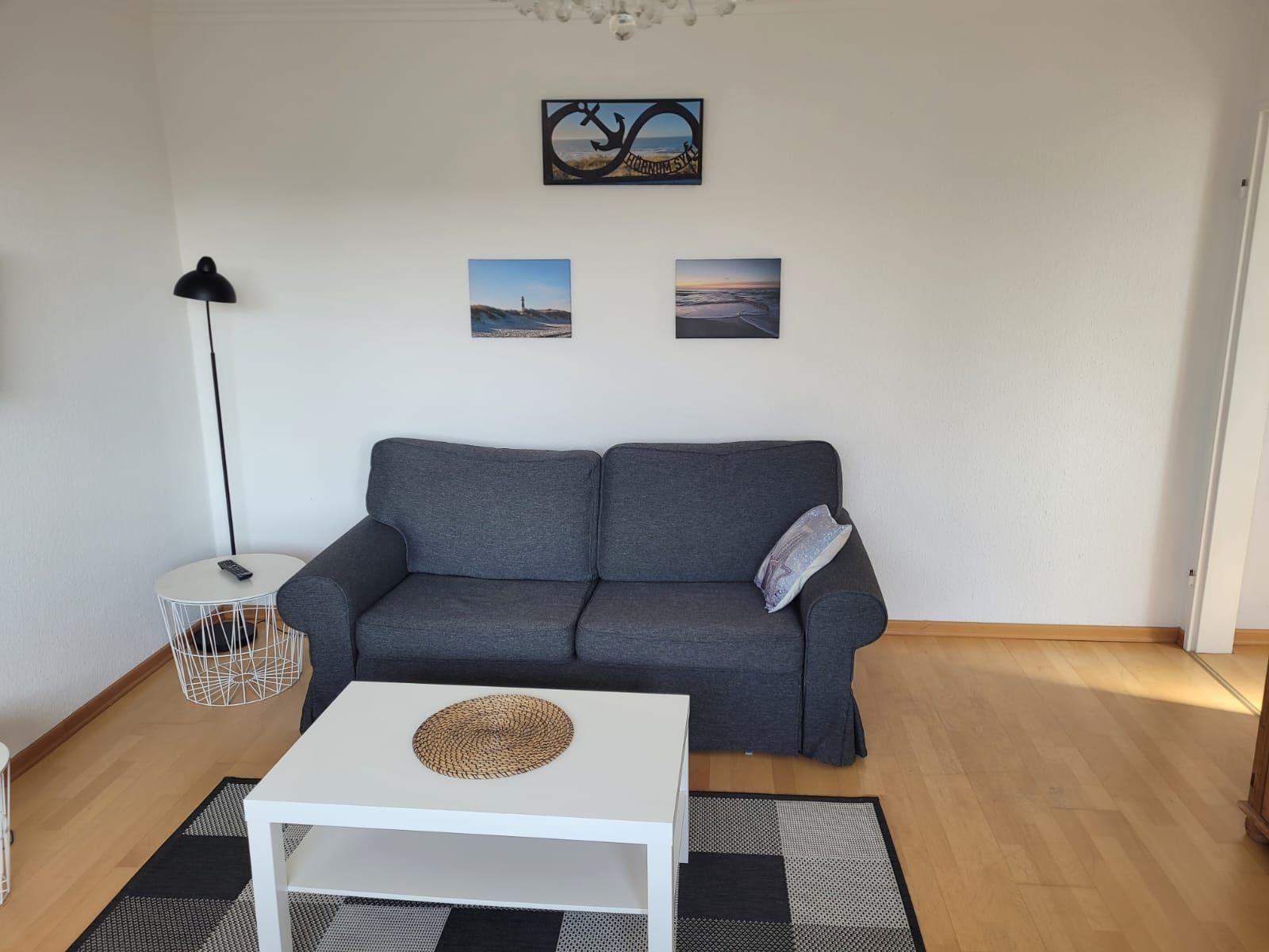 Ein Wohnzimmer mit grauem Sofa, weißem Couchtisch und Wandbildern mit Meeresmotiven.