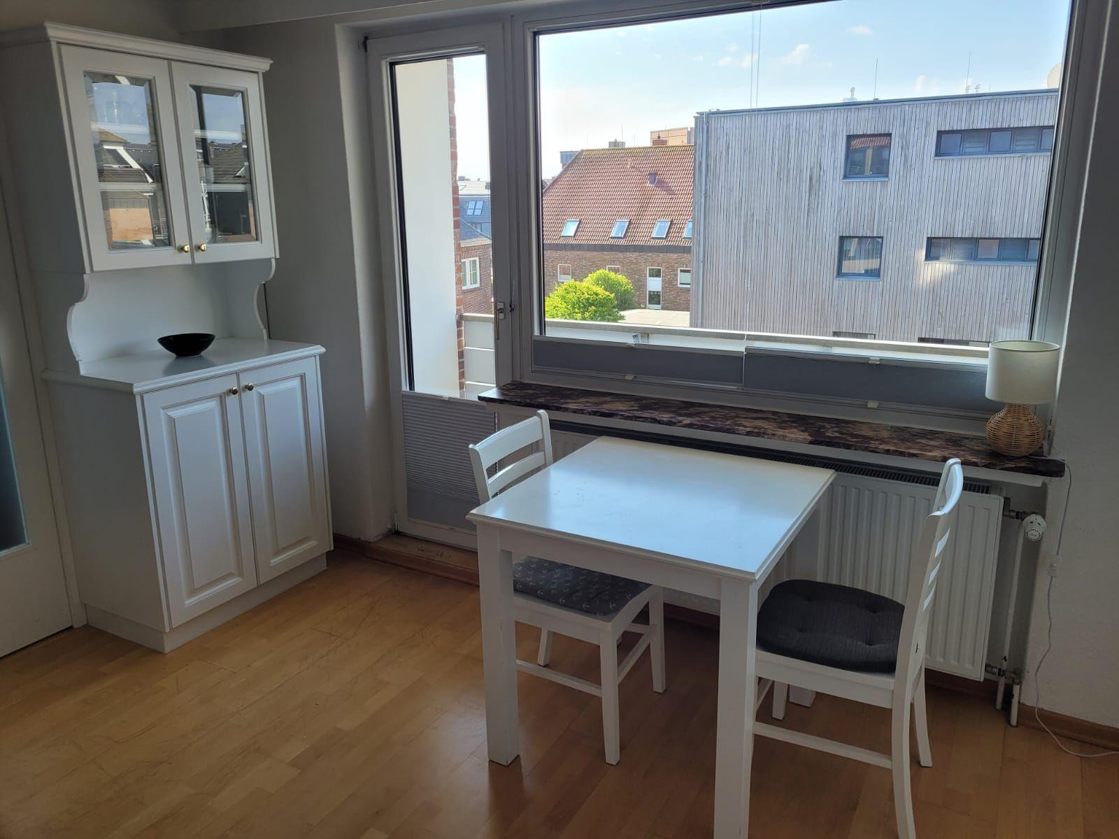 Esszimmer mit weißem Tisch, zwei Stühlen und Fensterblick auf Gebäude.