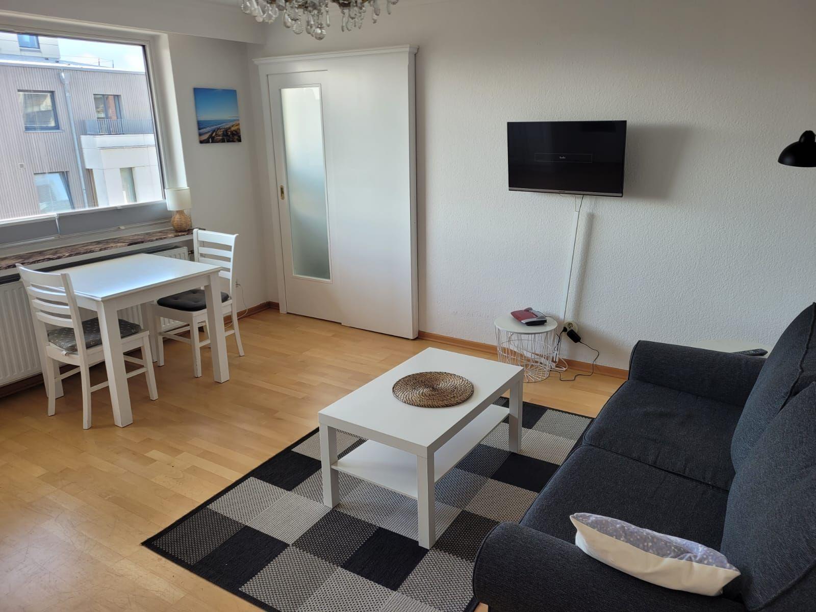 Wohn- und Essbereich mit Sofa, Tisch, Fernseher und Fenster.