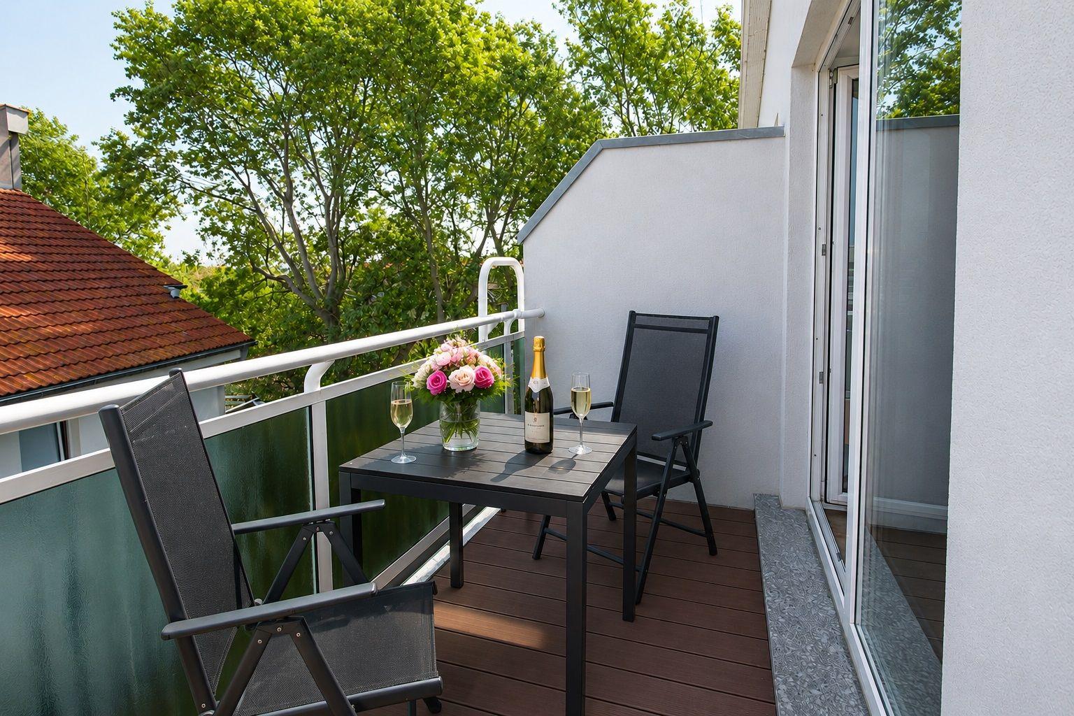 Terrasse mit Tisch, zwei Stühlen, Blumen und einer Flasche Champagner.