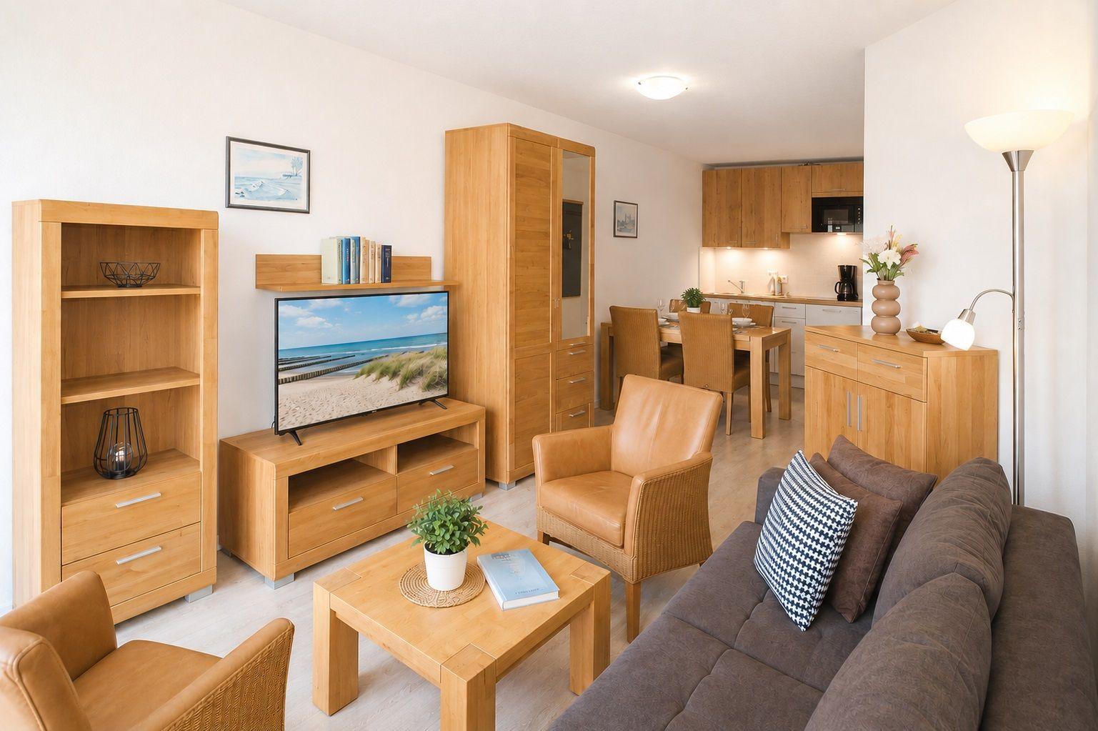 Wohn- und Essbereich mit Holzmöbeln, Sofa und Fernseher. Küche im Hintergrund.
