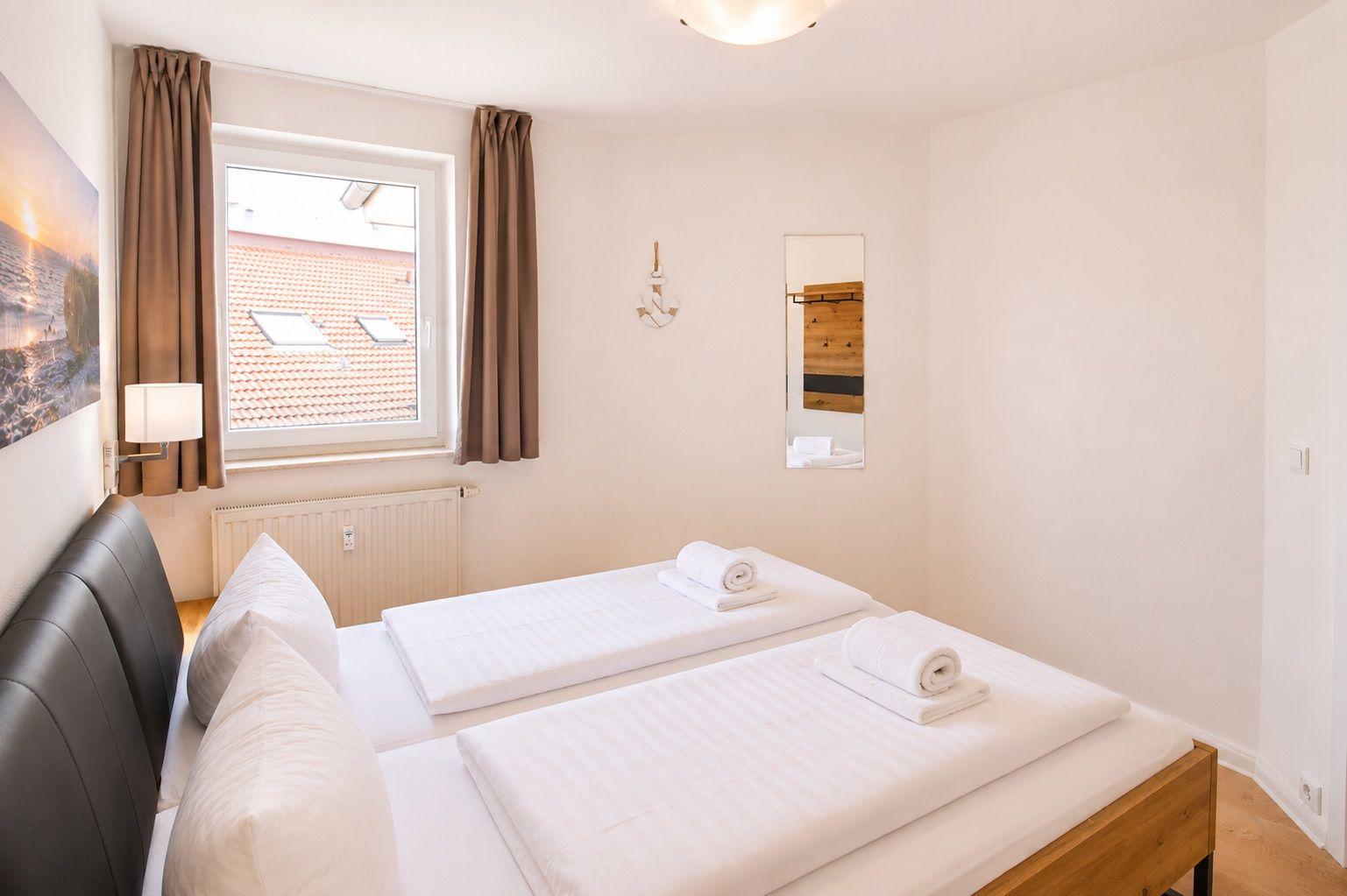 Zimmer mit Doppelbett, Fenster und Spiegel an der Wand.