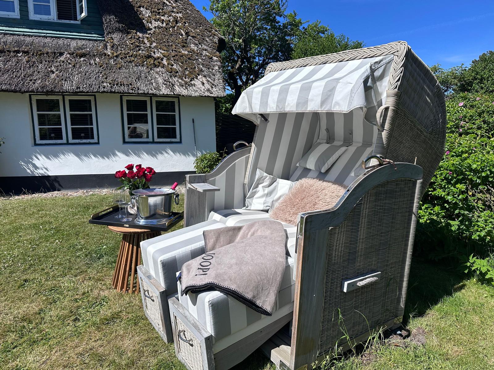 Hängesessel mit Sonnenschutz, Tisch mit Blumen und Kühler im Garten.