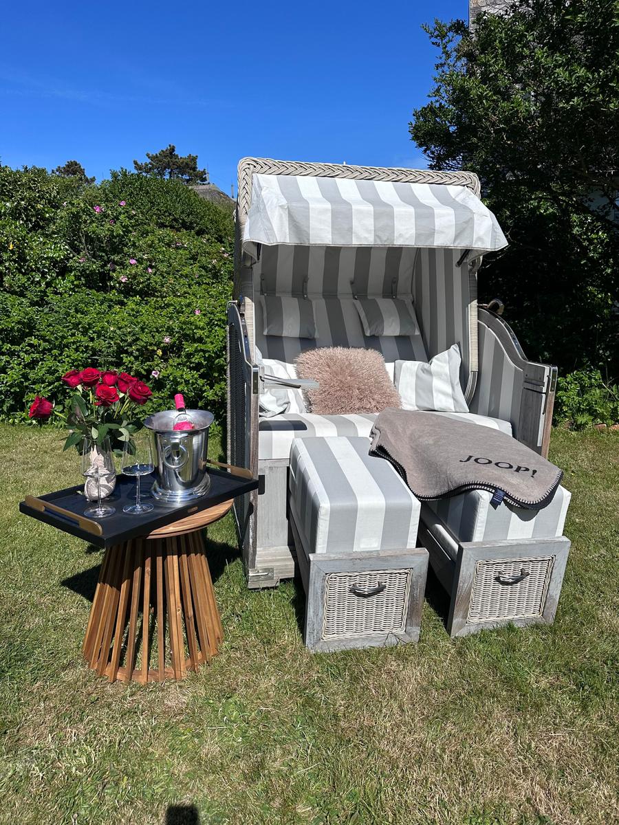 Strandkorb mit Kissen und Fußstützen auf Gras. Tisch mit Rosen und Champagner.