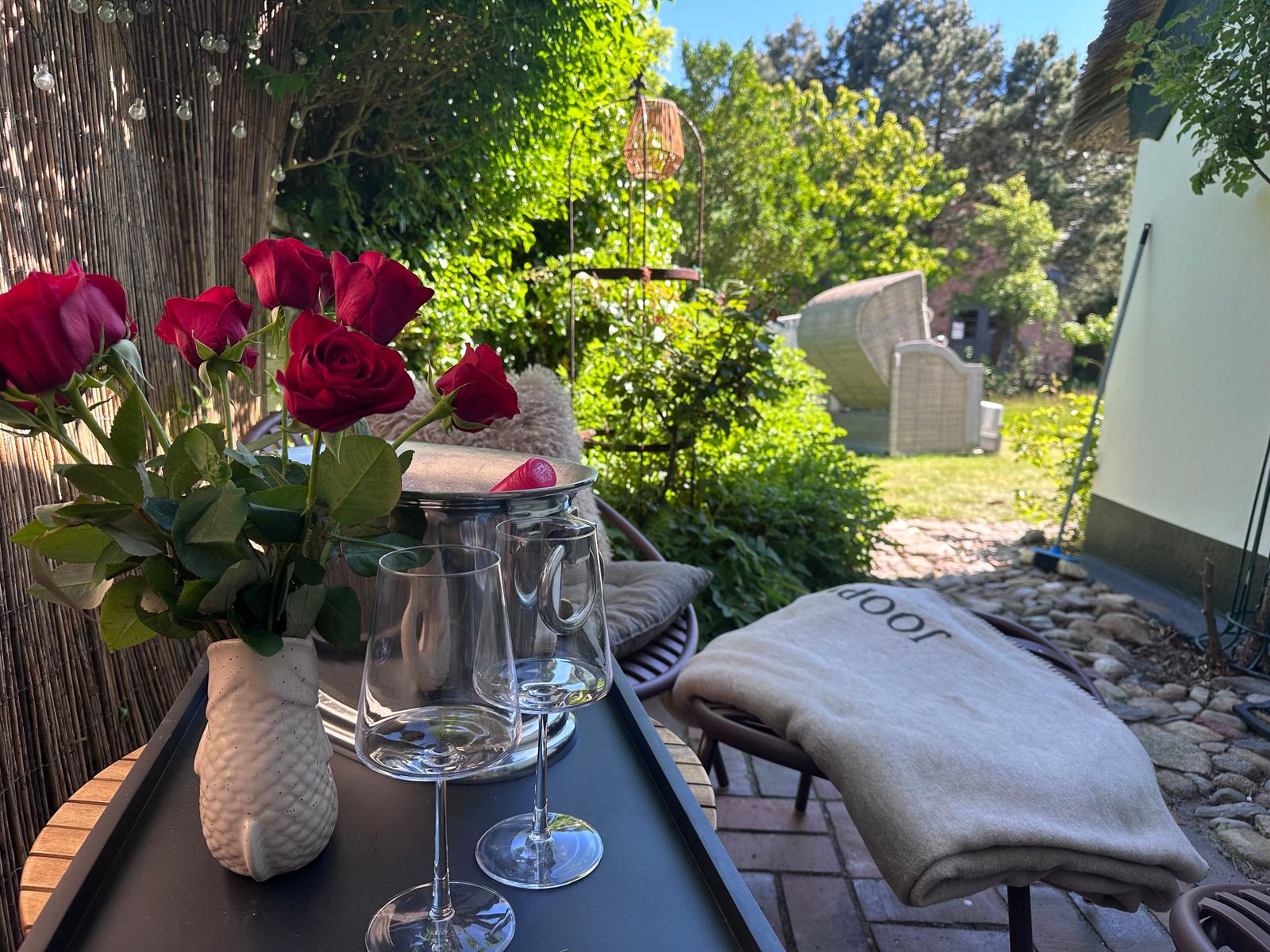 Tisch mit Rosen, Gläsern und Decke auf Terrasse mit Gartenblick.