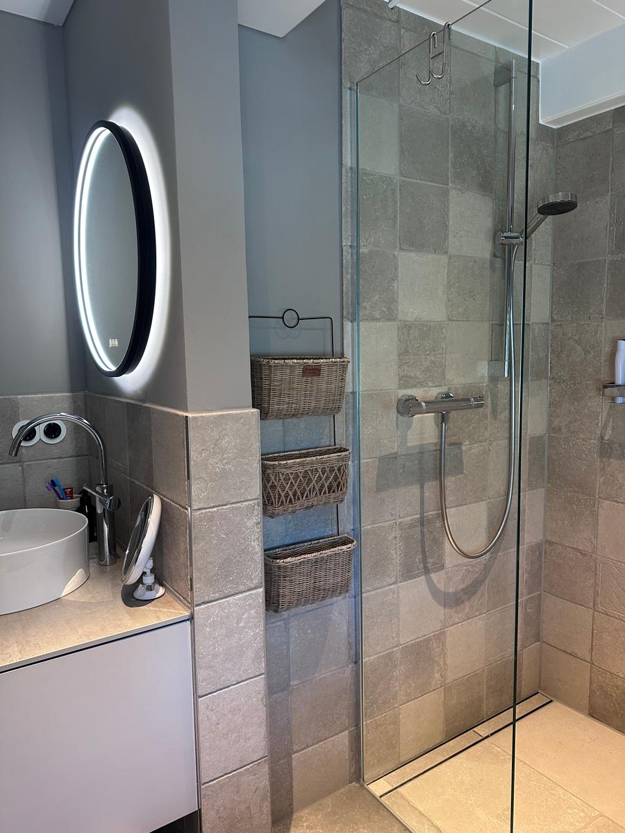 Badezimmer mit Dusche, Waschbecken und beleuchtetem Spiegel
