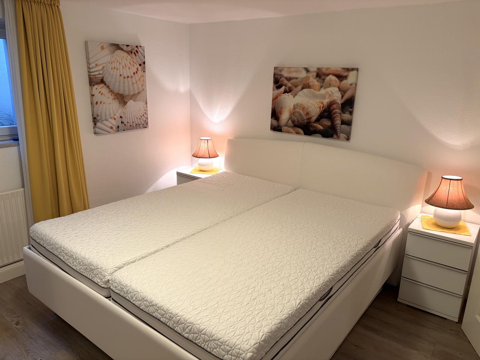 Schlafzimmer mit Doppelbett, zwei Nachttischen und Wandbildern mit Muscheln.