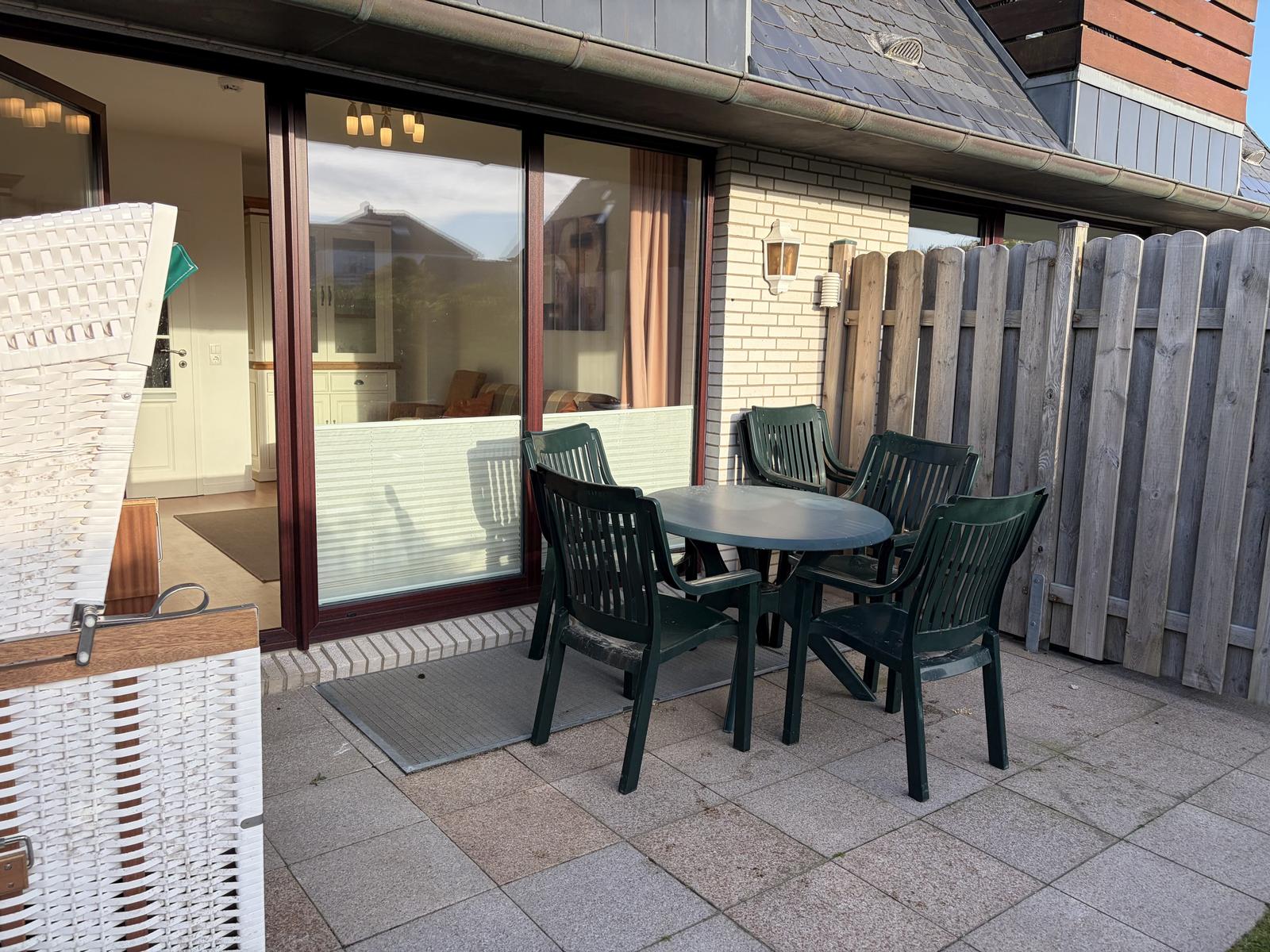 Terrasse mit Tisch und Stühlen, Sicht in Wohnraum über Glastür.