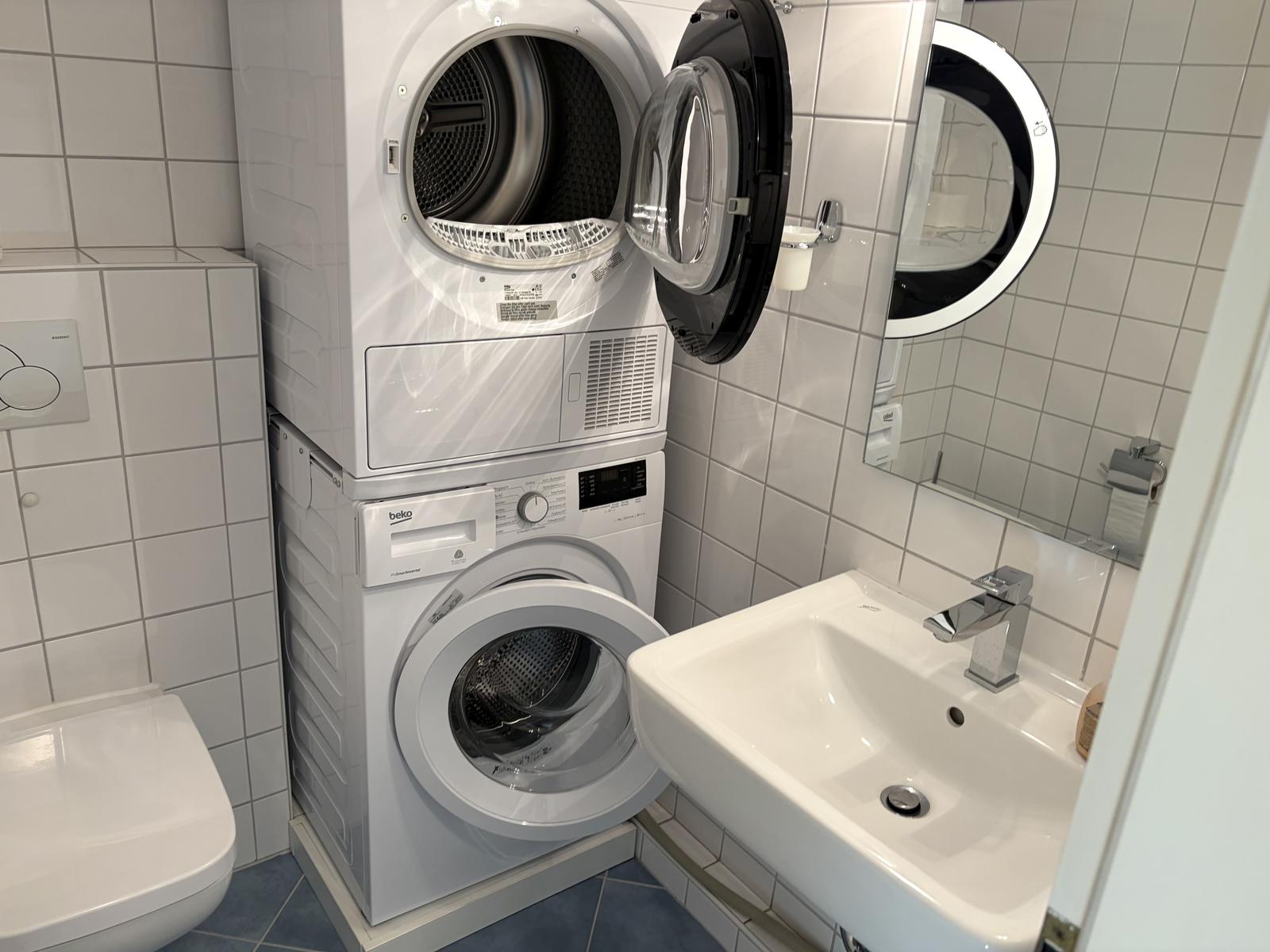 Waschmaschine und Trockner in weißer Küche mit Waschbecken und Spiegel.
