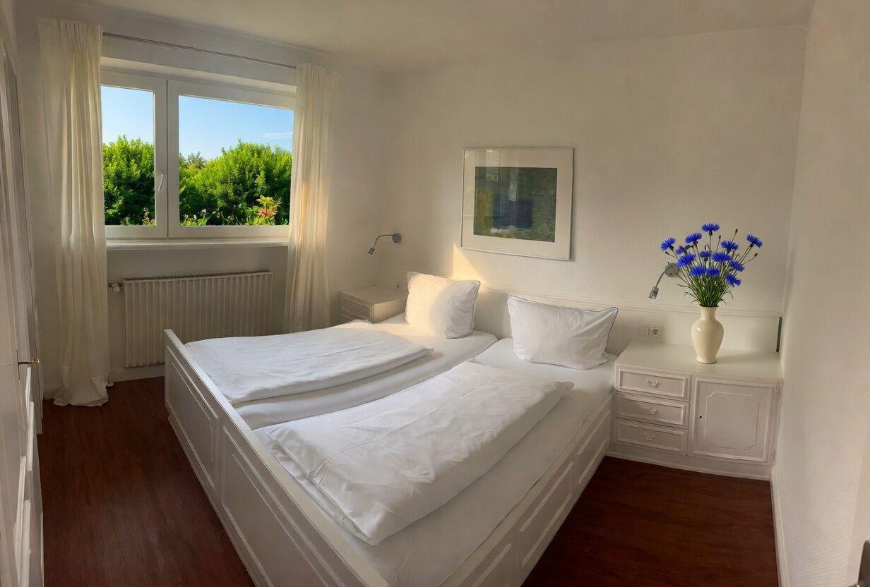 Schlafzimmer mit Doppelbett, Fenster und Blumenvase.