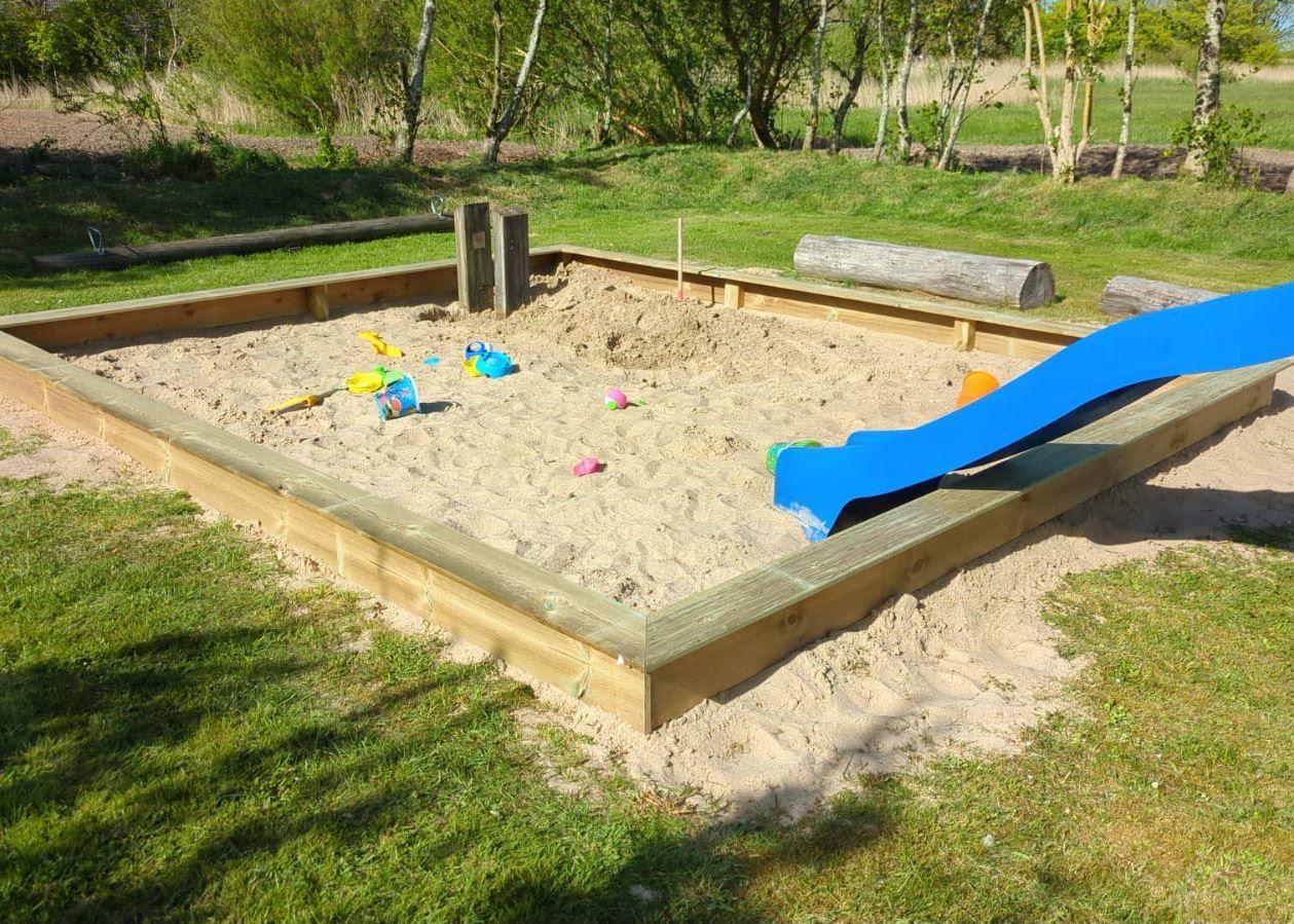 Ein Sandkasten mit blauer Rutsche und Spielzeug im Garten.