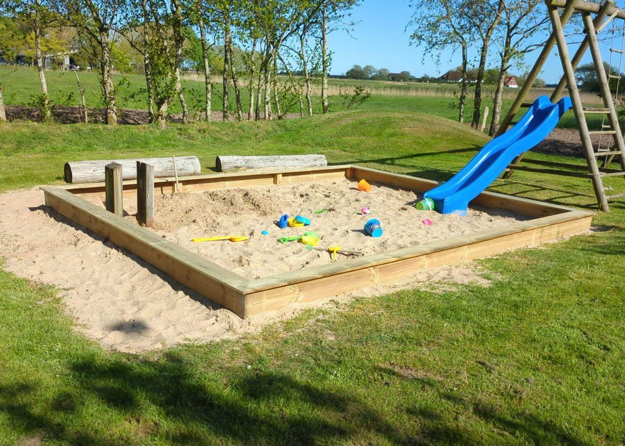 Holzrahmen-Sandkasten mit blauer Rutsche und Spielzeug im Garten.