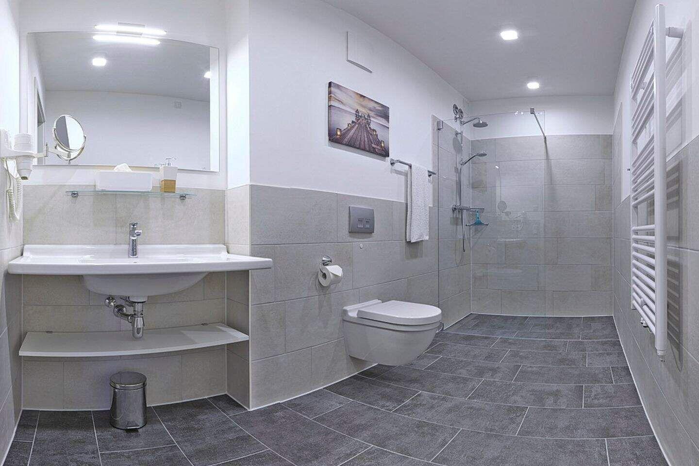 Badezimmer mit Dusche, Waschbecken und Toilette. Fliesenboden und Wandgestaltung.