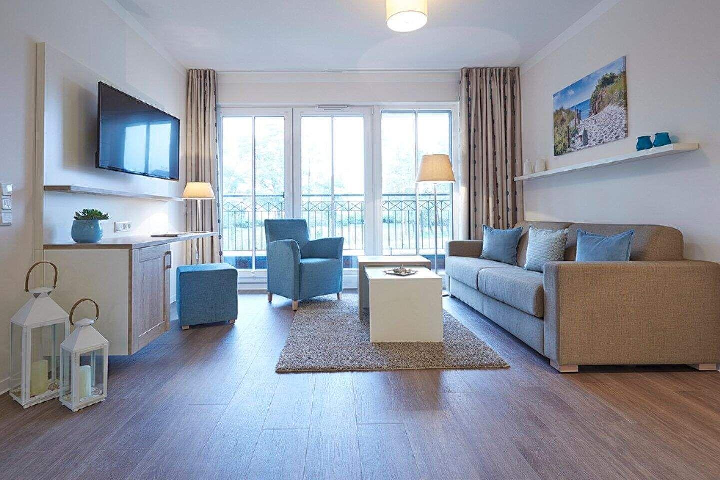 Wohnzimmer mit Sofa, Sessel und TV. Terrasse über große Fenster.