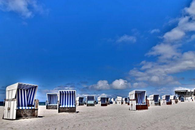 Strand mit blau-weißen Strandkörben unter blauem Himmel mit weißen Wolken.