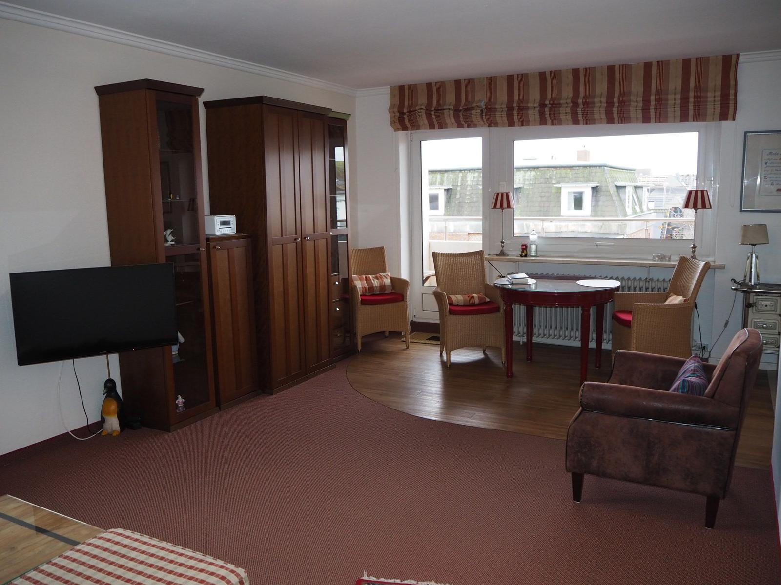 Wohnraum mit Fernseher, Schränken, Sitzgruppe und Fensterblick.