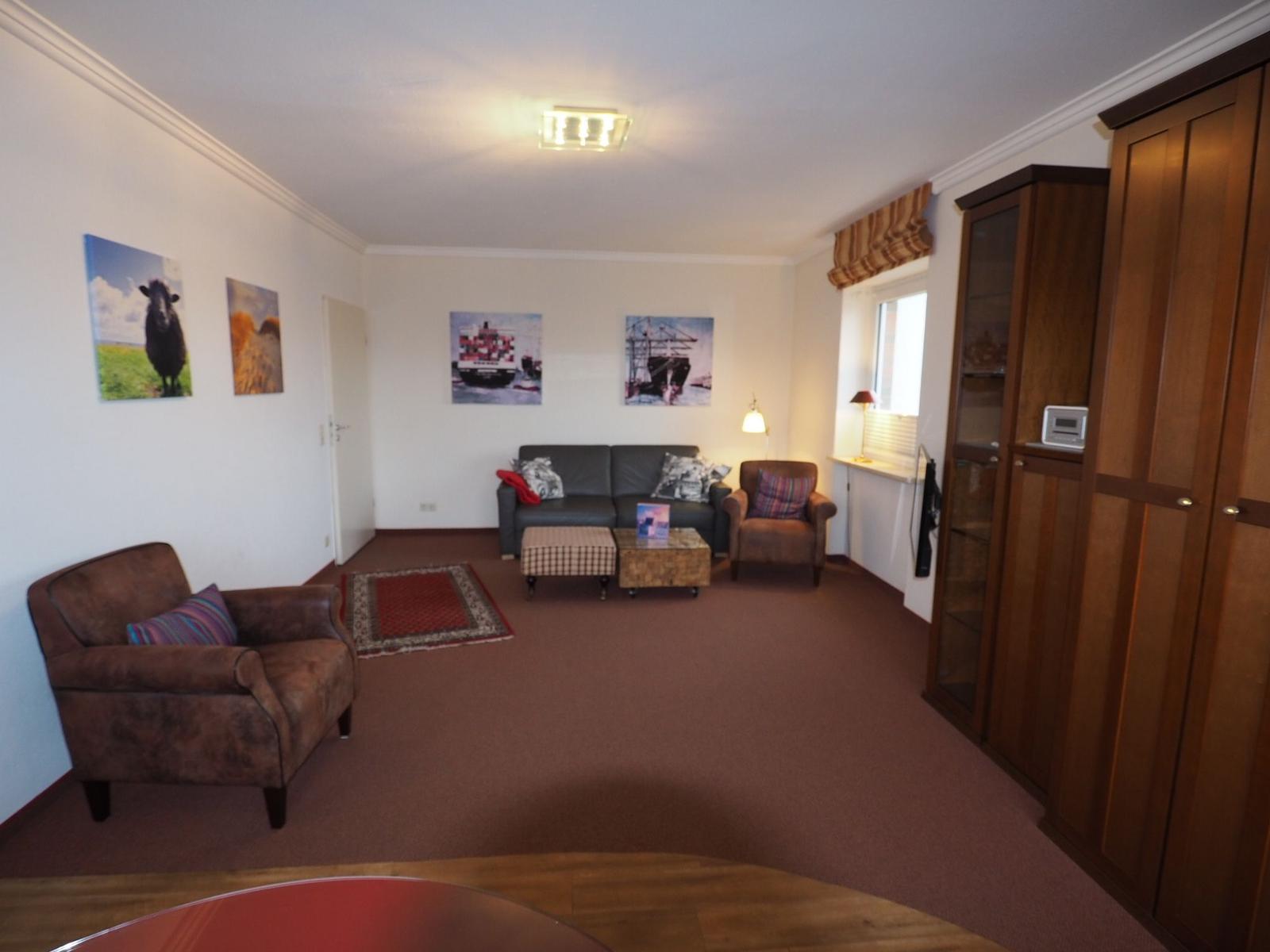 Wohnzimmer mit Sofa, zwei Sesseln, Teppich und Wandbildern.