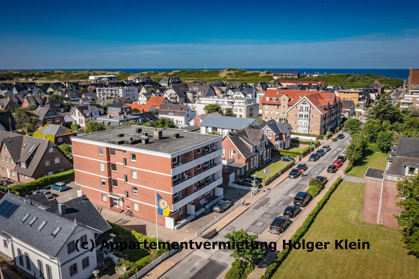 Aerial view of a coastal town with houses, streets, and the sea in the background.