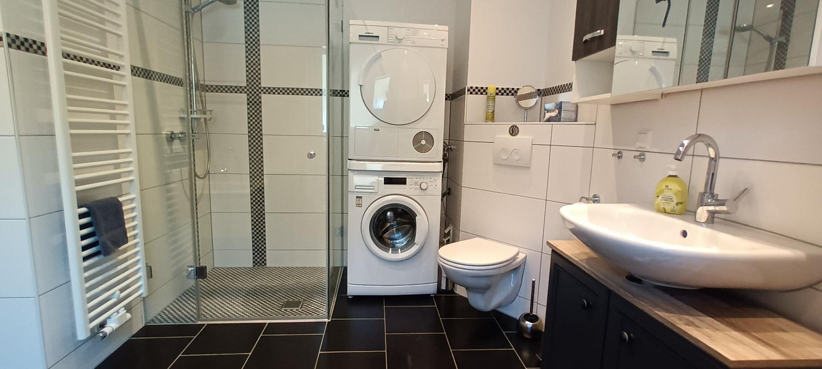 Badezimmer mit begehbarer Dusche, Badewanne, Waschmaschine und Trockner und Zugang zum Balkon
