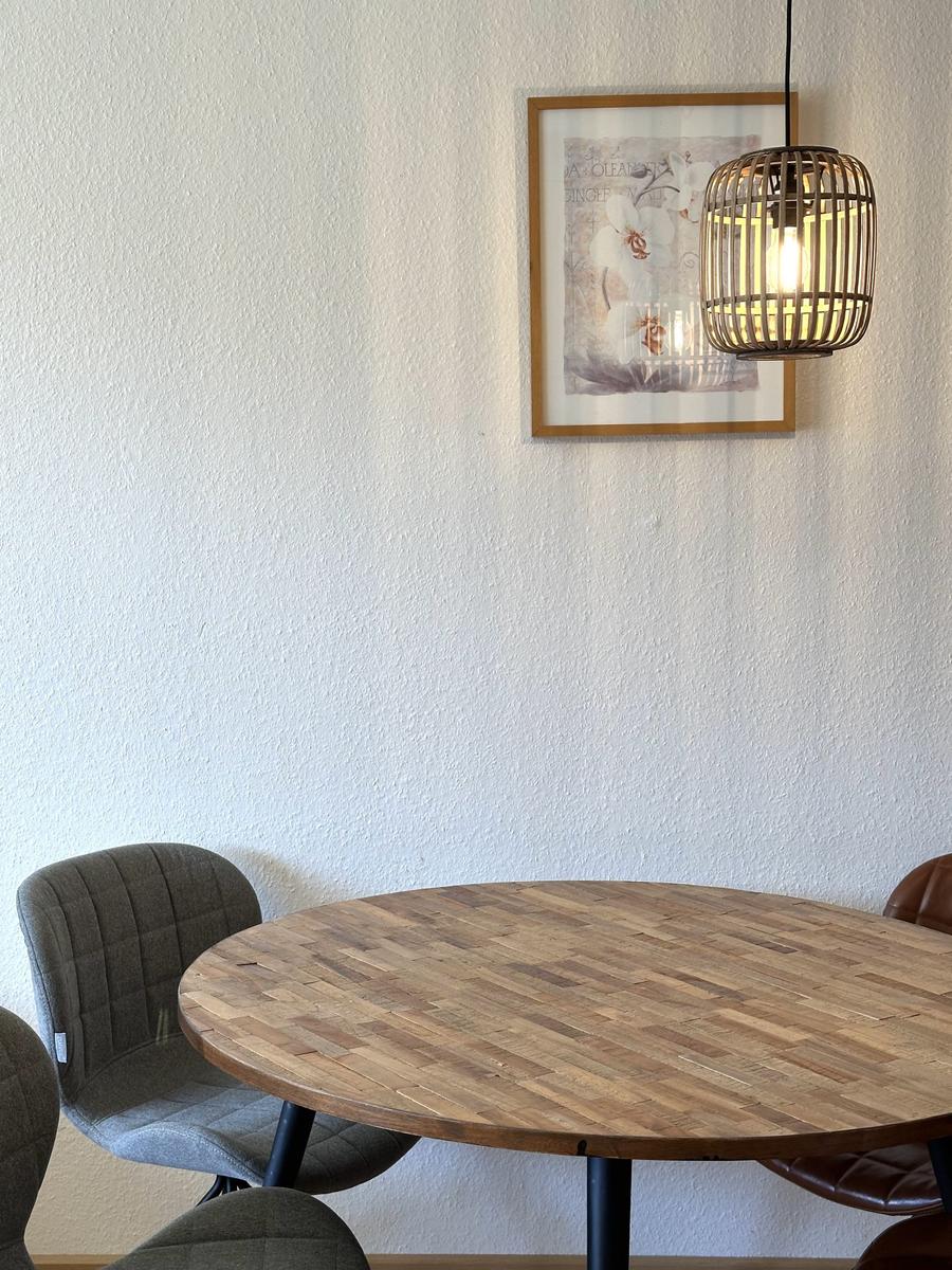 Runder Holztisch mit Stühlen unter einer Pendelleuchte an der Wand.